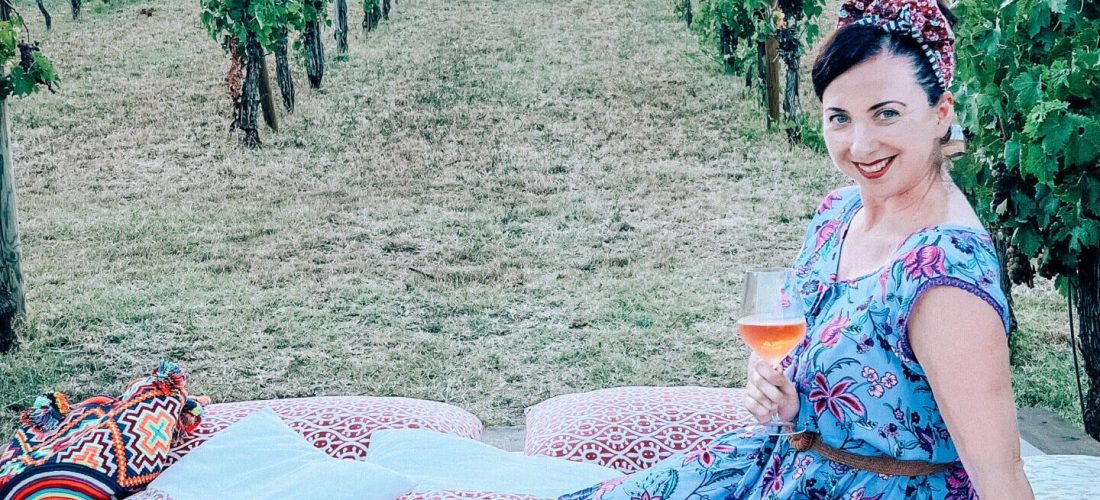 Ragazza che fa picnic con calice di vino in mano, seduta su lettini di fronte ai vigneti a Ravenna